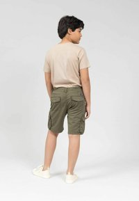 Shorts cargo kaki avec poches latérales, en tissu mélangé coton, associés à un t-shirt beige uni et des baskets blanches, vus de dos.