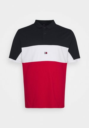 Koszulka polo z czarnym górnym pasem, białym środkowym paskiem z małym logo, czerwonym dołem i krótkimi rękawami, rozłożona na płasko na białym tle.