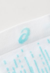 White sock with turquoise accents, featuring a textured surface, a small logo, and scattered patterned details across the fabric.