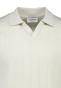 Krämfärgad polo skjorta med ribbad krage och texturerat zickzackmönster. Har en V-hals och en avslappnad passform. Varumärkesetikett synlig.