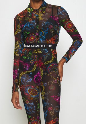 Langærmet bodysuit i gennemsigtigt sort stof med livlige flerfarvede mønstre og en mærket talje, der læser "VERSACE JEANS COUTURE."