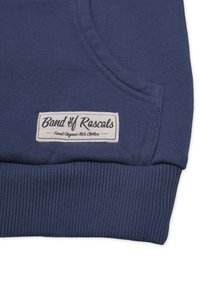 Tummansininen huppari, jossa on ribbireunat hihoissa ja helmassa. Sisältää kankaisen tarran, jossa lukee "Band of Rascals" valkoisella tekstillä. Valmistettu orgaanisista materiaaleista.