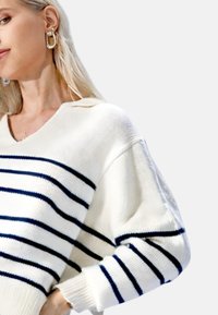 Hvit genser med marineblå horisontale striper, V-halsdesign, myk teksturert stoff, oversized passform og ribbestrikkede mansjetter.