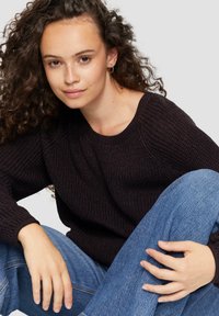 Dunkel gestrickter Pullover mit rundem Halsauschnitt und langen Ärmeln. Modell trägt blaue Jeans aus Denim, die eine lockere Passform und gelebte Textur zeigen.