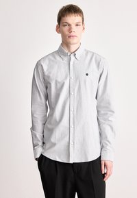 Πουκάμισο με κουμπιά και ρίγες σε γκρι και λευκό. Διαθέτει κλασικό γιακά, μακριά μανίκια και μικρό μαύρο λογότυπο στο στήθος. Υλικό από βαμβάκι.