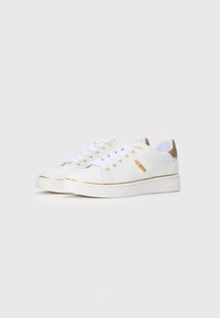 Hvite sneakers med gullaccenter, laget av glatt materiale, rund tå, flat såle, og fremtredende merkevare på siden og tungen.