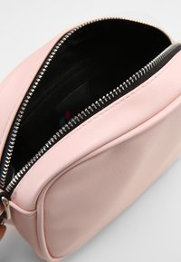 Borsa a tracolla in pelle rosa chiaro con zip argentata parzialmente aperta, che mostra l'interno in tessuto nero.