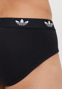 Svart bomullsboxer med vit märkets midjeband som har tre ränder och en trebladig logotyp. Slät textur och figurnära design.
