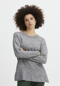 Pull en tricot gris avec une coupe décontractée, un col rond et un ourlet côtelé. Texture douce, manches longues et un dos légèrement plus long.