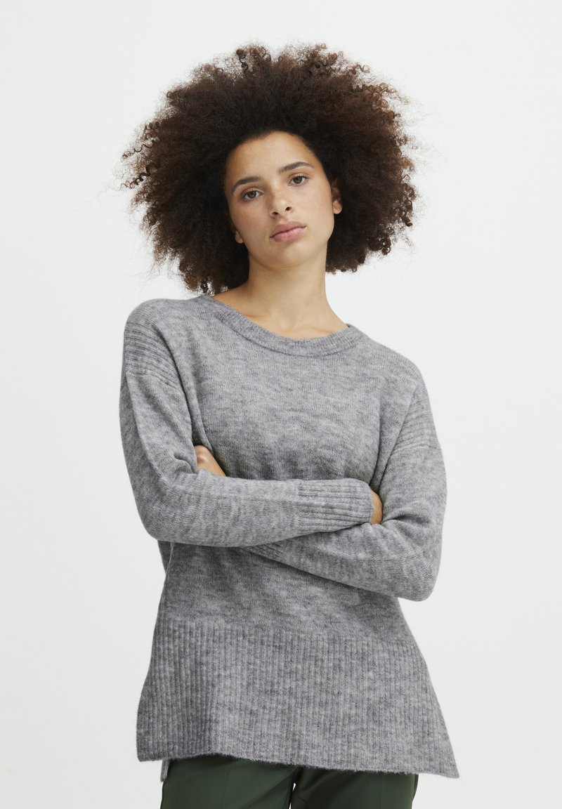 Pull en tricot gris avec une coupe décontractée, un col rond et un ourlet côtelé. Texture douce, manches longues et un dos légèrement plus long.