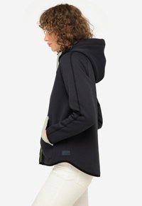 Felpa con cappuccio grigia scura con cuciture nere, tasche foderate in fleece e un orlo curvo. Presenta un piccolo logo sul lato.