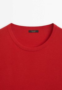 Pull rouge à col rond avec une étiquette noire cousue à l'intérieur du col sur un fond blanc.