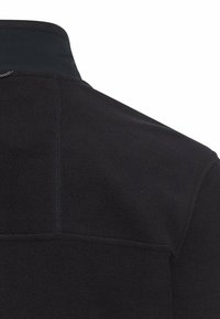 Schwarze Fleecejacke mit hohem Kragen, strukturierter Oberfläche und dezenten Steppnähten auf der Rückseite. Weiches Material sorgt für zusätzlichen Tragekomfort.