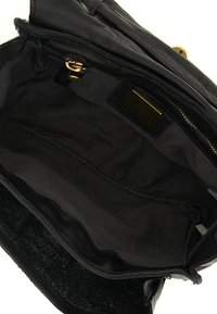 Interno di una borsa a mano in pelle nera con una fodera testurizzata, hardware dorato, tasca con zip e un piccolo etichetta fissata all'interno.