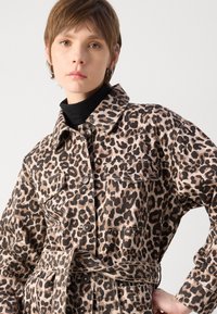 Veste en imprimé léopard beige et noir, avec un col, des poches avant, des boutonnières et une taille ceinturée.