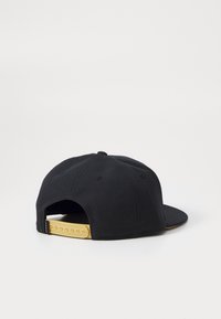 Cappellino snapback nero con una cinghia gialla regolabile, adagiato piatto con la parte posteriore rivolta verso l'alto su una superficie bianca semplice.