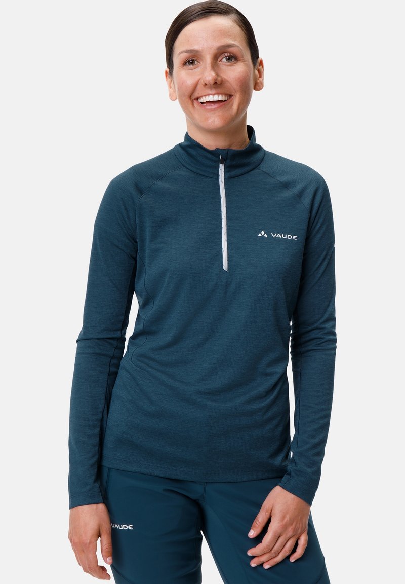 Pull-over long à manches, couleur teal foncé, avec un col haut et un zip mi-hauteur ; présente un logo sur la poitrine et un tissu texturé. Associé à un pantalon assorti.