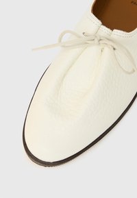 Chaussure en cuir blanc avec un bout arrondi, une surface texturée et une fine semelle marron. Disposant de lacets assortis et de détails de couture minimalistes.