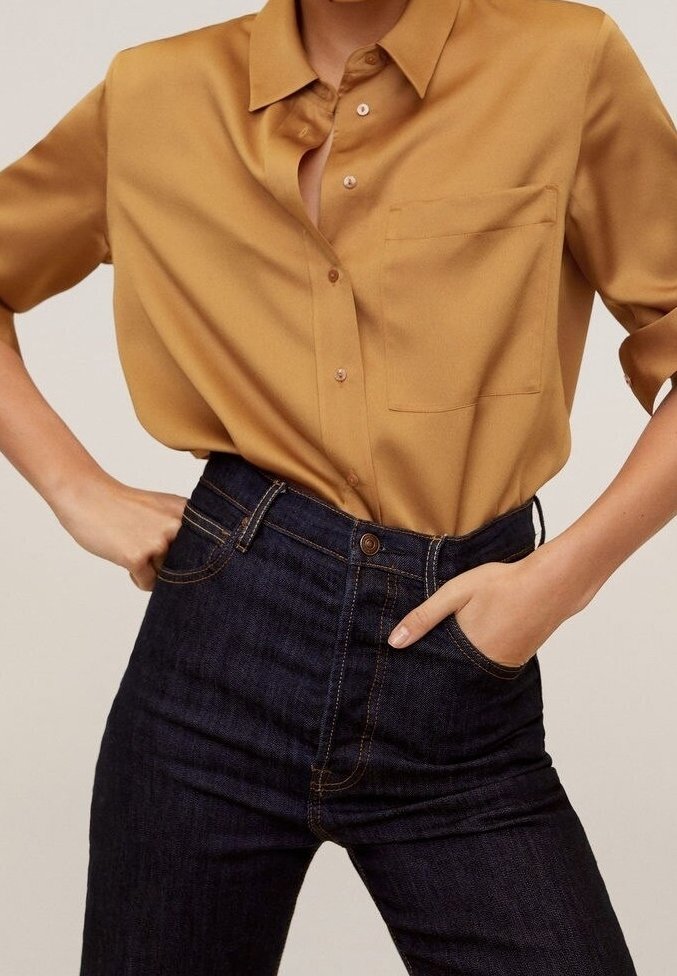 Chemise à manches courtes jaune moutarde avec col boutonné et poche avant, associée à un jean en denim foncé taille haute avec des coutures dorées.