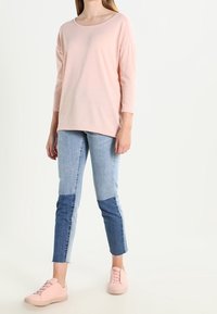 Helles rosa Langarmoberteil mit rundem Halsausschnitt; kombiniert mit Jeans in Patchwork-Optik mit verschiedenen Blautönen; hellrosa Sneaker.