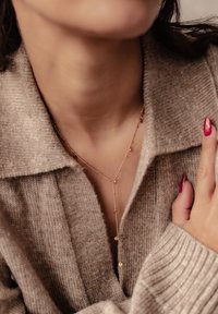 Collier en pendentif en or avec une chaîne délicate, au design minimaliste, comportant de petits médaillons ronds. Porté sur un vêtement en tricot beige.