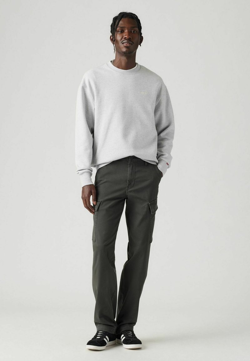 Grauer Sweatshirt mit Rippbündchen, kombiniert mit olivgrünen Cargo-Hosen mit Seitentaschen. Schwarze Sneakers mit weißen Sohlen runden den Look ab.