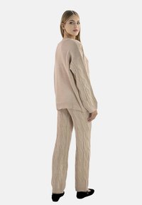 Beige gestrickter Pullover mit Zopfmuster, oversized geschnitten, kombiniert mit passenden Zopfmuster-Hosen; weiche Textur und lässige Silhouette.