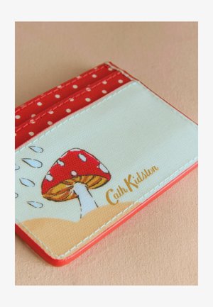 Sarkans punktiņs karšu turētājs ar krēmveida virsmu, kurā redzams sarkana sēne un "Cath Kidston" iefrēzēts zeltā. Gluda tekstūra.