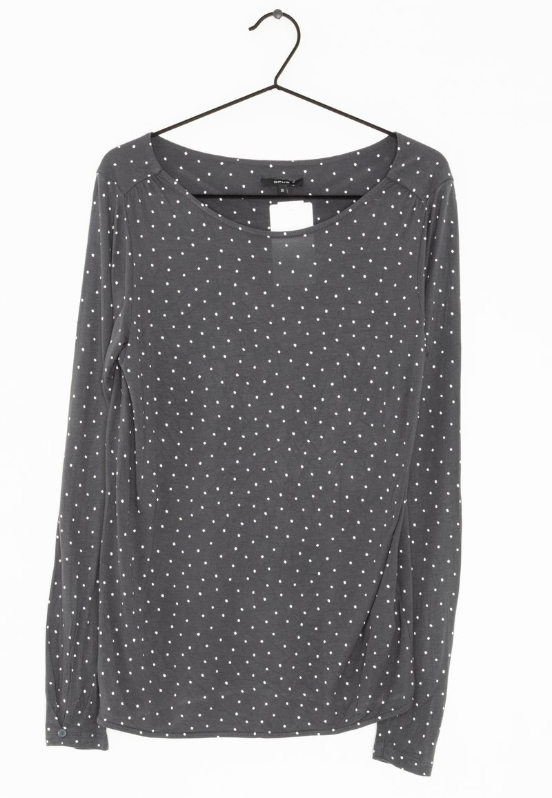 Chemise à manches longues gris foncé avec des pois blancs accrochée à un cintre noir sur fond blanc.