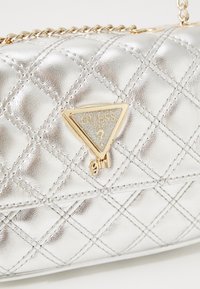 Zilveren, gewatteerde handtas van metallic materiaal met een driehoekig logo voorzien van glitters en gouden accenten. Inclusief kettingband.