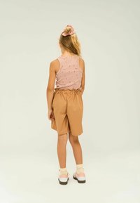 Top a maniche lunghe rosa chiaro a coste con motivo floreale, abbinato a pantaloni corti beige con vita arricciata. Scarpe bianche con dettagli rosa completano il look.