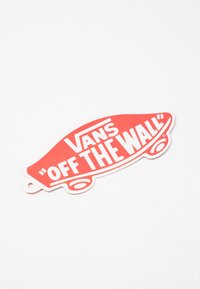 Etichetta del logo "Off The Wall" dei Red Vans, a forma di skateboard, con caratteri bianchi in grassetto e un piccolo foro per il fissaggio. Design piatto, superficie liscia.
