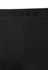 Boxer de algodón negro con cintura texturizada que muestra una marca en relieve, diseñados para comodidad y ajuste. Superficie lisa sin patrones.