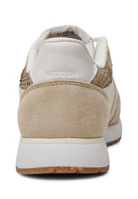 Beige-weißer Sneaker von hinten gesehen, mit Wildleder, strukturiertem Stoff und einem geprägten "WODEN"-Logo auf der Fersenschlaufe.