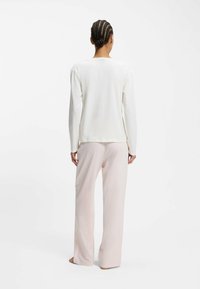 Biały top z długim rękawem w połączeniu z jasnoróżowymi, szerokimi spodniami. Top ma luźny krój i zaokrąglony dekolt, wykonany jest z gładkiego materiału.