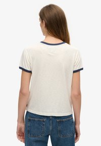 Cremefarvet t-shirt med korte ærmer og marineblå ribkant ved halsudskæringen og ærmerne. Blødt, letvægts materiale med en afslappet pasform, der har et synligt mærke på bagsiden.