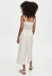 Lichtgekleurde jumpsuit met dunne banden, een geraffineerde taille en wijde, cropped broekspijpen. De stof heeft subtiele verticale strepen en kantaccenten.