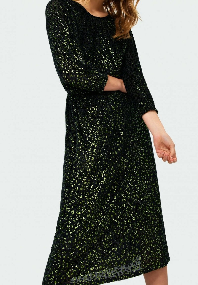 Robe noire à manches trois-quarts avec un motif imprimé animal vert, mi-longue, taille froncée et texture transparente.