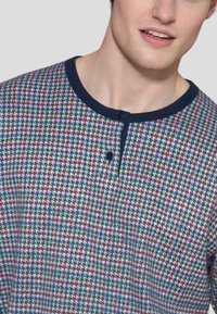 Camicia a motivi multicolori con scollatura rotonda, caratterizzata da una finitura blu navy e due bottoni. Il tessuto ha un aspetto tessuto e testurizzato.