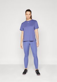 T-shirt de sport violet à manches courtes et fentes sur les côtés, associé à un legging violet assorti, avec une coupe ajustée et des baskets noires sportives.