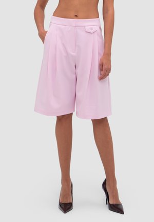 Vrouwentorso en benen met een high waist, loszittende pastelroze knielange short met plooien aan de voorkant en zwarte puntige hakken.