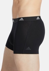Calzoncillos bóxer negros hechos de un material suave y elástico, con una cintura negra que presenta el logo de Adidas en blanco. Marca sutil en la pierna.