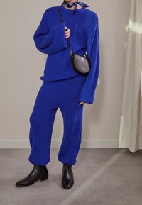 Pull bleu tricoté à larges manches avec un motif texturé, accompagné d'un pantalon assorti. Porté avec des bottines noires et un petit sac noir.