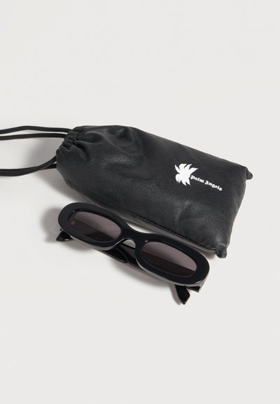 Lunettes de soleil ovales noires avec des verres foncés à côté d'une pochette noire à cordon avec un logo palmier blanc et le texte "palm angels".