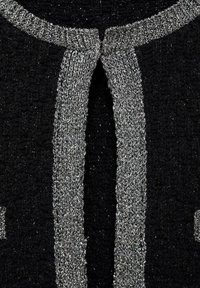 Tissu tricoté noir avec une bordure métallique argentée le long d'un devant ouvert et du décolleté, montrant une couture texturée détaillée.