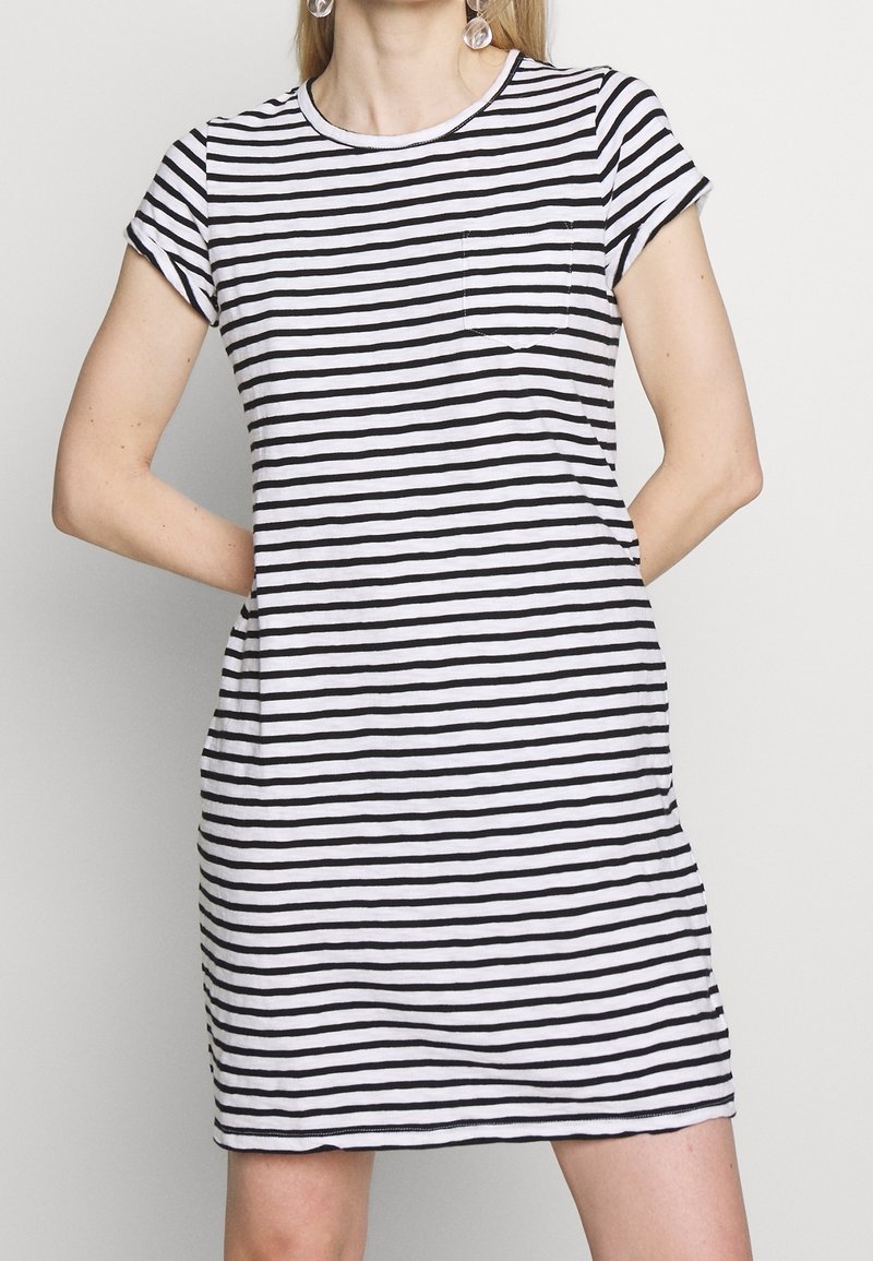 Robe T-shirt rayée en coton noir et blanc, avec des manches courtes retroussées, un col rond et une poche avant sur le côté gauche.