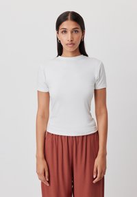 T-shirt bianca a maniche corte, aderente, con scollatura rotonda, realizzata in tessuto morbido, abbinata a pantaloni larghi marroni. Design semplice e moderno.