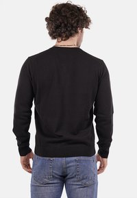 Maglione nero a maglia con maniche lunghe e polsini a coste. La parte posteriore presenta un collo rotondo e una texture liscia, abbinato a jeans blu.