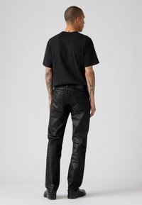 Camiseta de algodón negra combinada con vaqueros de denim oscuros y ligeramente brillantes. Los vaqueros tienen un corte recto y bolsillos traseros visibles.