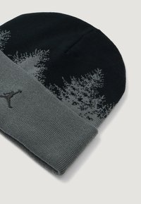 Črna in siva pletena kapa z manšeto, ki ima gradientni vzorec in �črno logotipno podrobnost. Izdelana je iz mehkega, raztegljivega materiala.